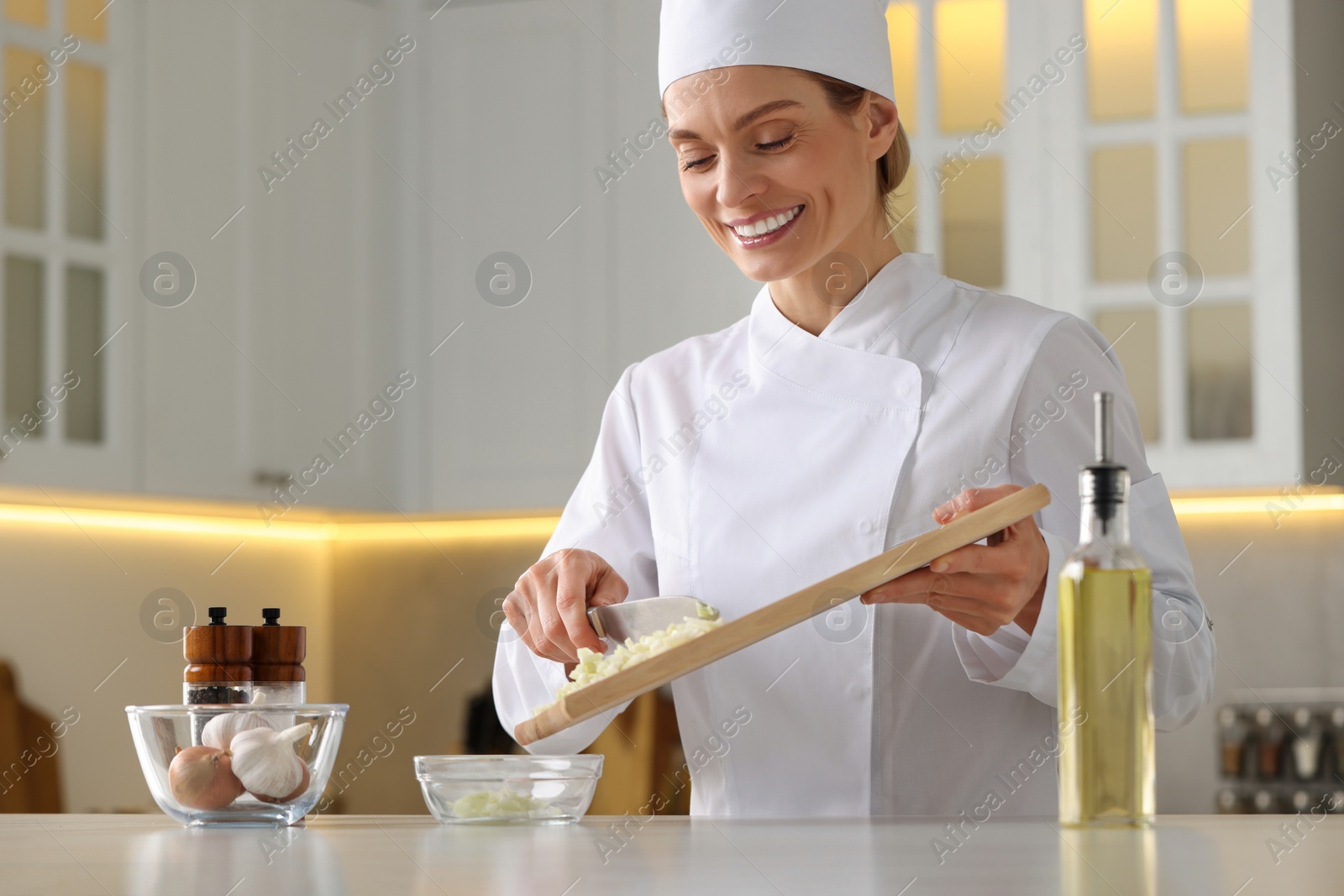 Photo of Professional chef putting cut onion into bowl at white marble table indoors, low angle view