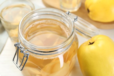 Photo of Delicious quince drink in glass jar and fresh fruits on table, closeup