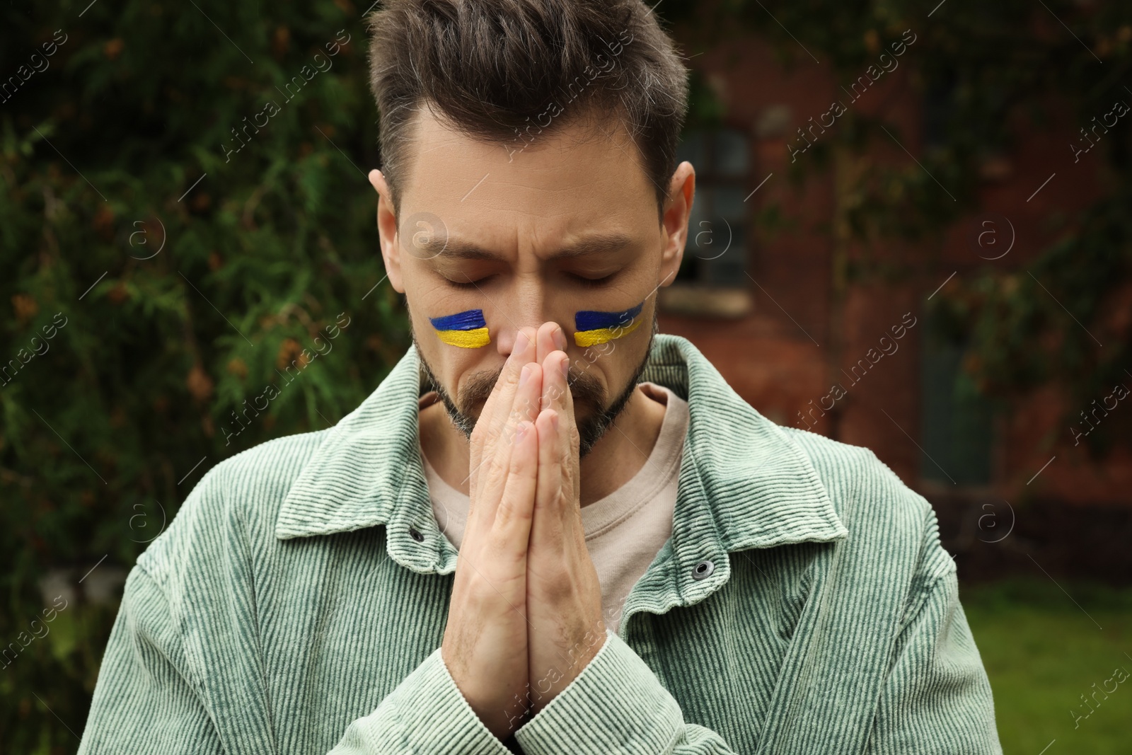 Photo of Sad man with drawings of Ukrainian flag on face outdoors