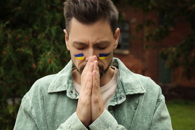 Sad man with drawings of Ukrainian flag on face outdoors