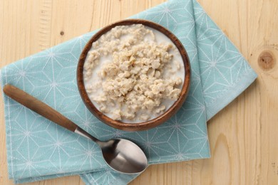 Photo of Tasty boiled oatmeal in bowl and spoon on wooden table, top view