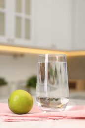 Photo of Filtered water in glass and lime on white marble table in kitchen, closeup