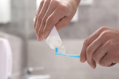 Photo of Man squeezing toothpaste from tube onto toothbrush in bathroom, closeup