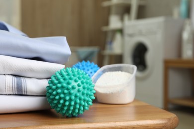 Photo of Dryer balls near stacked clean clothes and detergent on wooden table in laundry room. Space for text