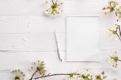 Photo of Guest list. Notebook, pen and spring tree branches with beautiful blossoms on white wooden background, flat lay. Space for text