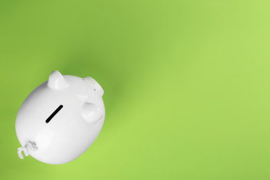 Photo of White piggy bank on green background, top view. Space for text