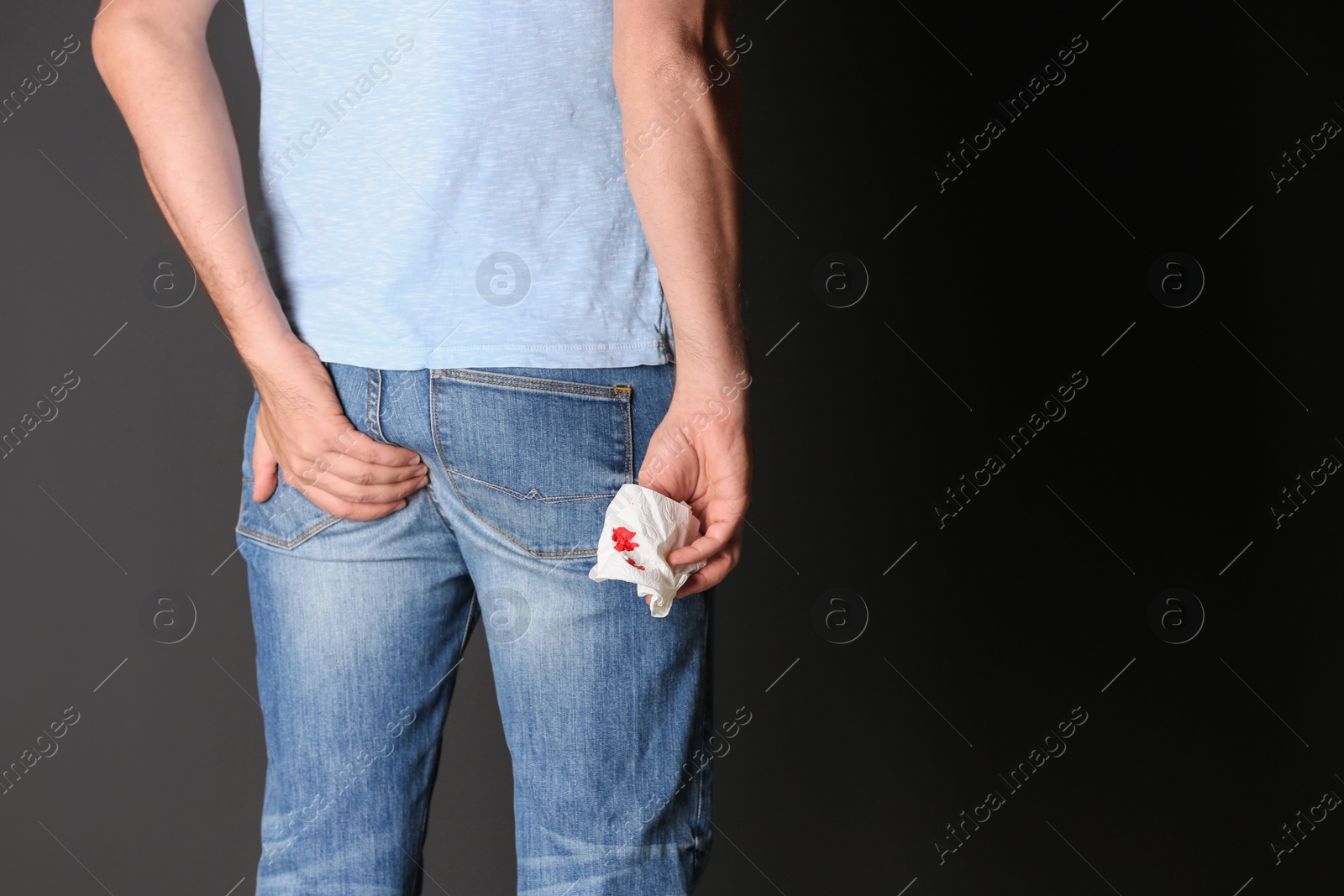 Photo of Man holding toilet paper with blood stain on black background, space for text. Hemorrhoid concept