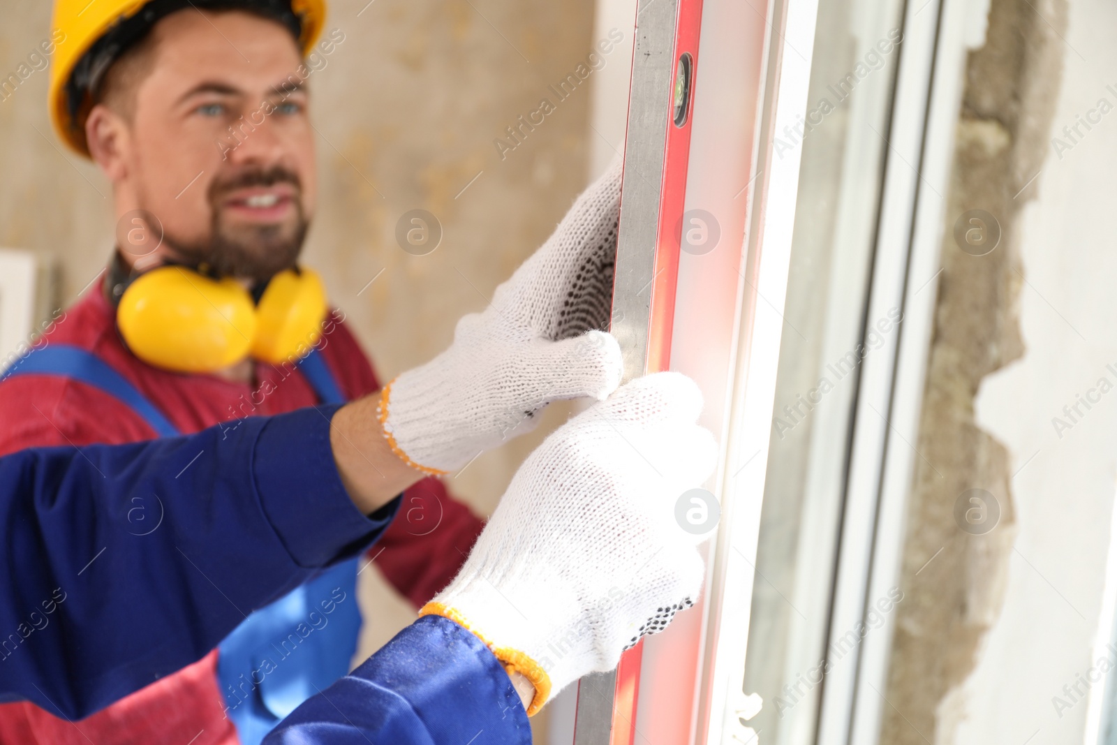 Photo of Workers using bubble level for installing window indoors, closeup