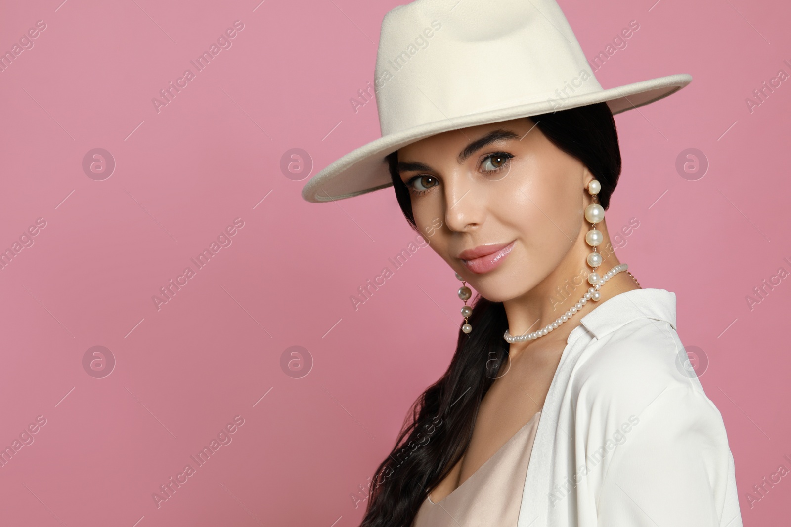 Photo of Young woman wearing elegant pearl jewelry on pink background, space for text