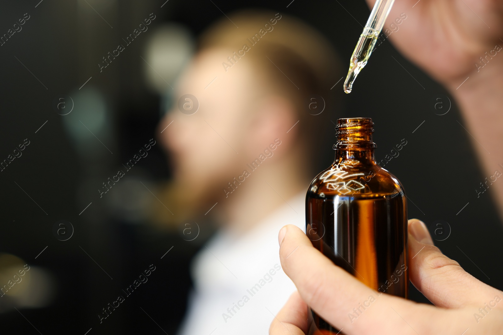 Photo of Hairdresser holding bottle of beard oil in barbershop, closeup with space for text. Professional shaving service