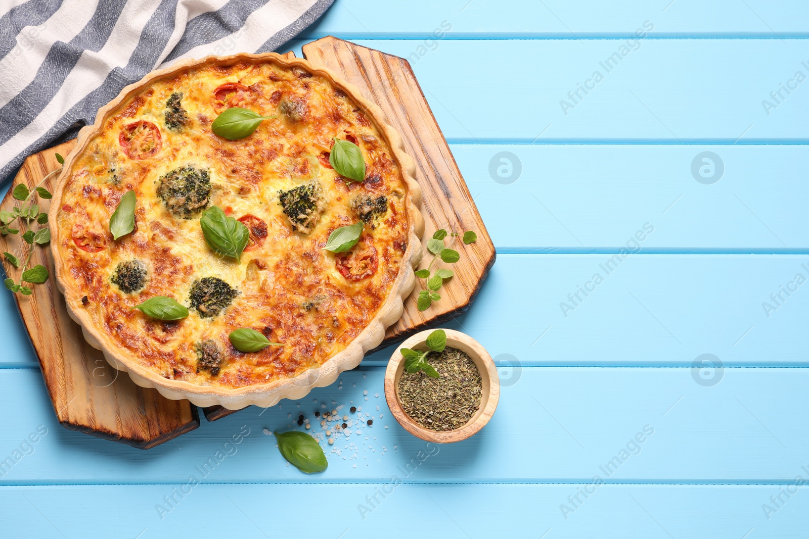 Photo of Delicious homemade vegetable quiche and seasoning on light blue wooden table, flat lay. Space for text