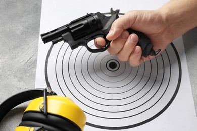 Photo of Man with handgun near shooting target and headphones on table, closeup