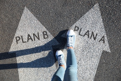 Choosing between Plan A and Plan B. Woman near arrows on road, above view