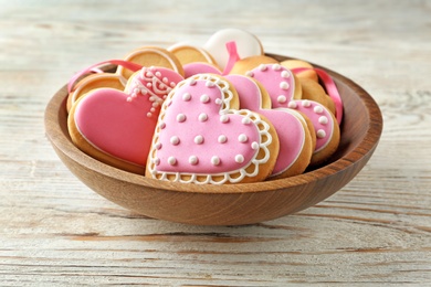 Photo of Bowl with decorated heart shaped cookies on wooden table