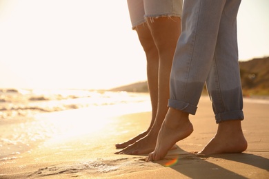 Photo of Couple on sandy beach near sea at sunset, closeup of legs