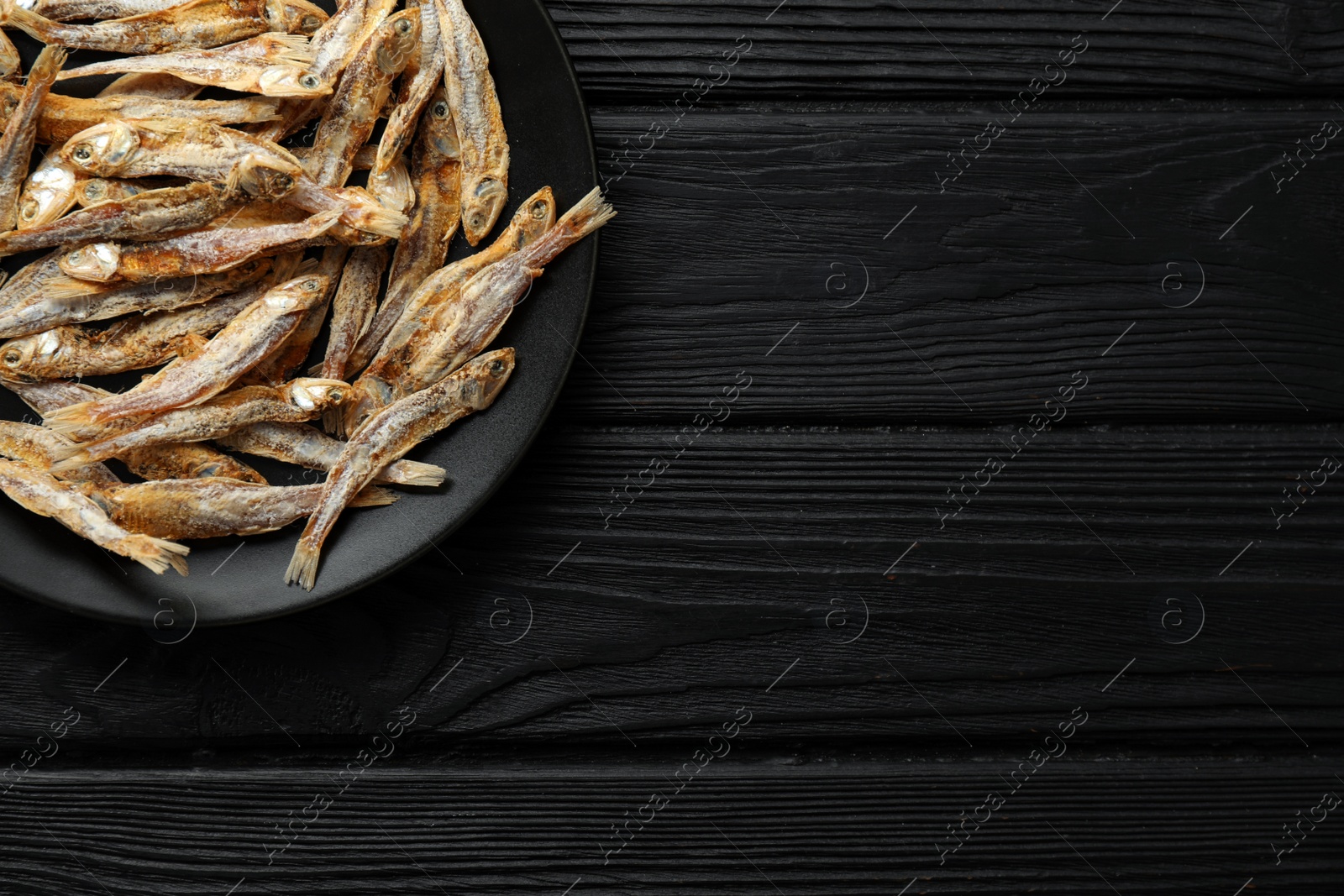 Photo of Delicious dried anchovies on black wooden table, top view. Space for text