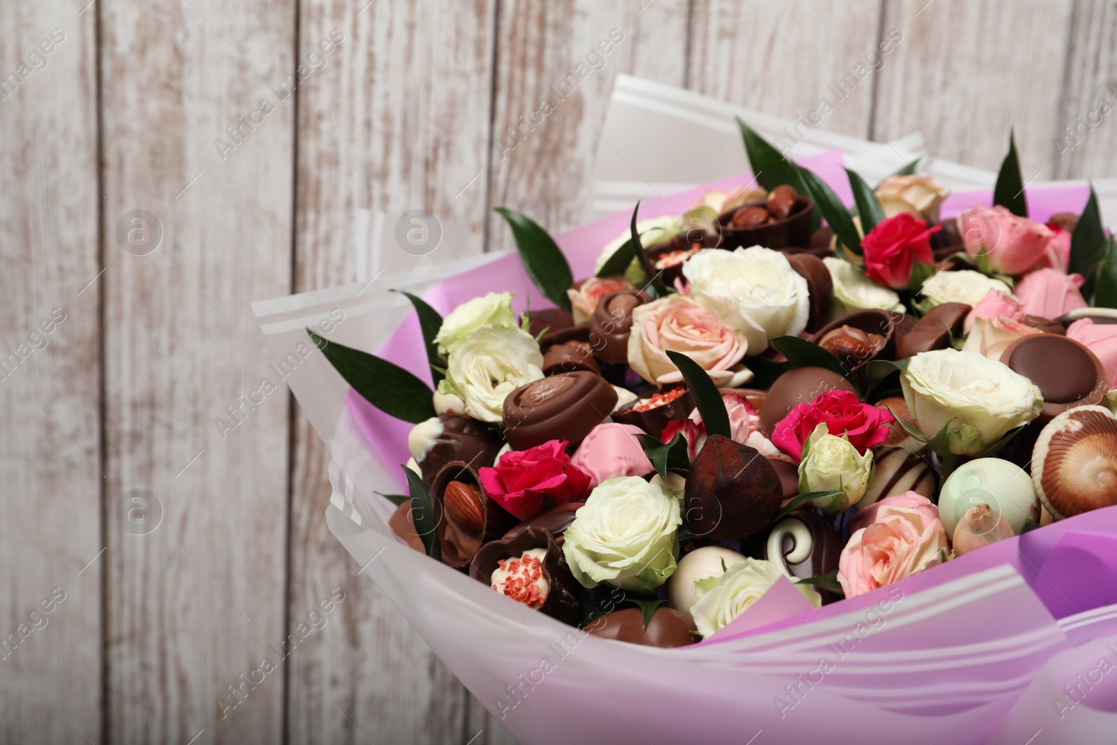 Photo of Beautiful bouquet of flowers and chocolate candies on white wooden background, closeup
