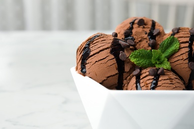 Photo of Bowl of chocolate ice cream with syrup and mint on table, closeup