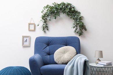 Photo of Stylish room decorated with beautiful eucalyptus garland above comfortable armchair
