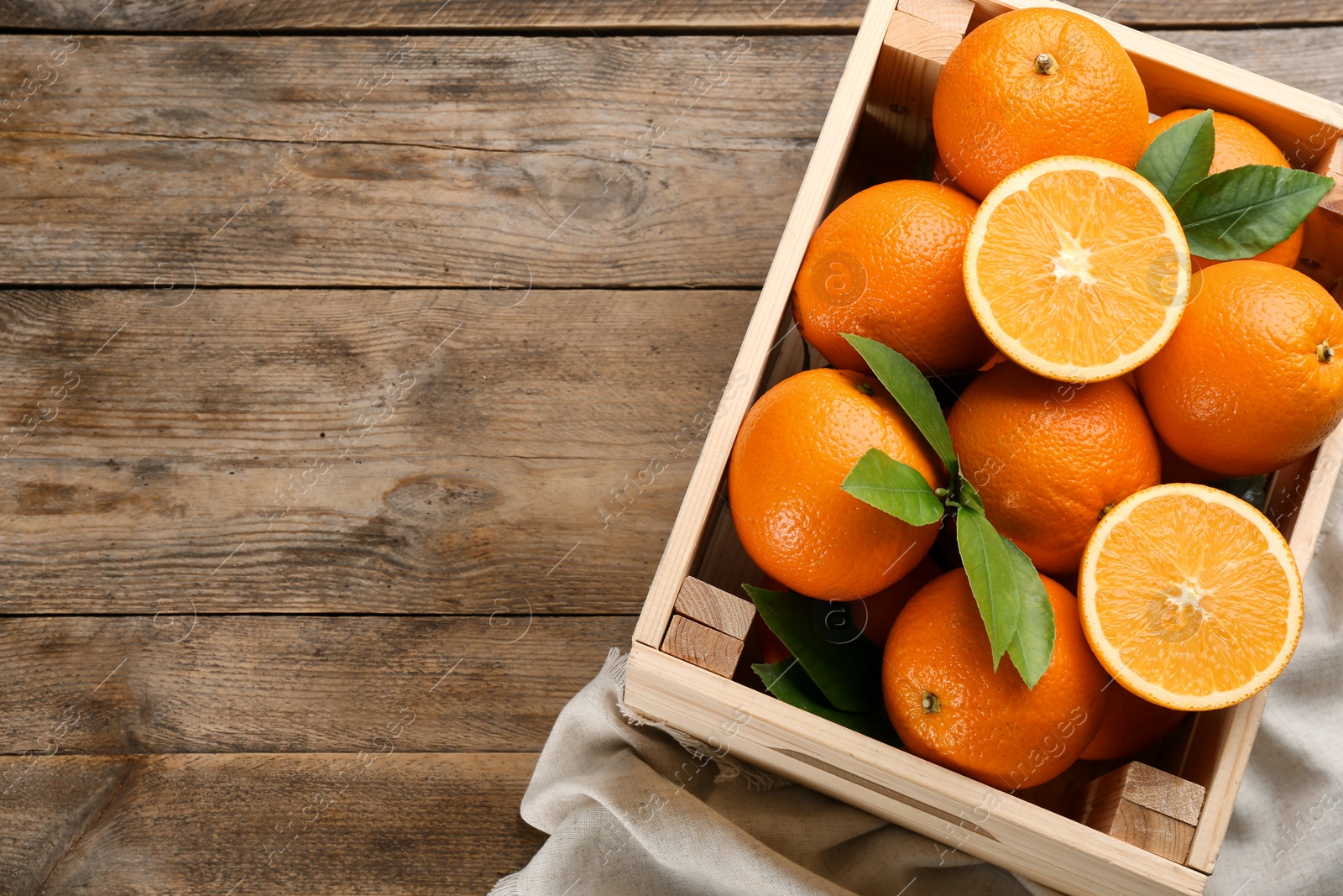 Photo of Delicious ripe oranges in crate on wooden table, top view. Space for text