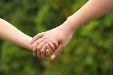 Photo of Woman and child holding hands outdoors, closeup