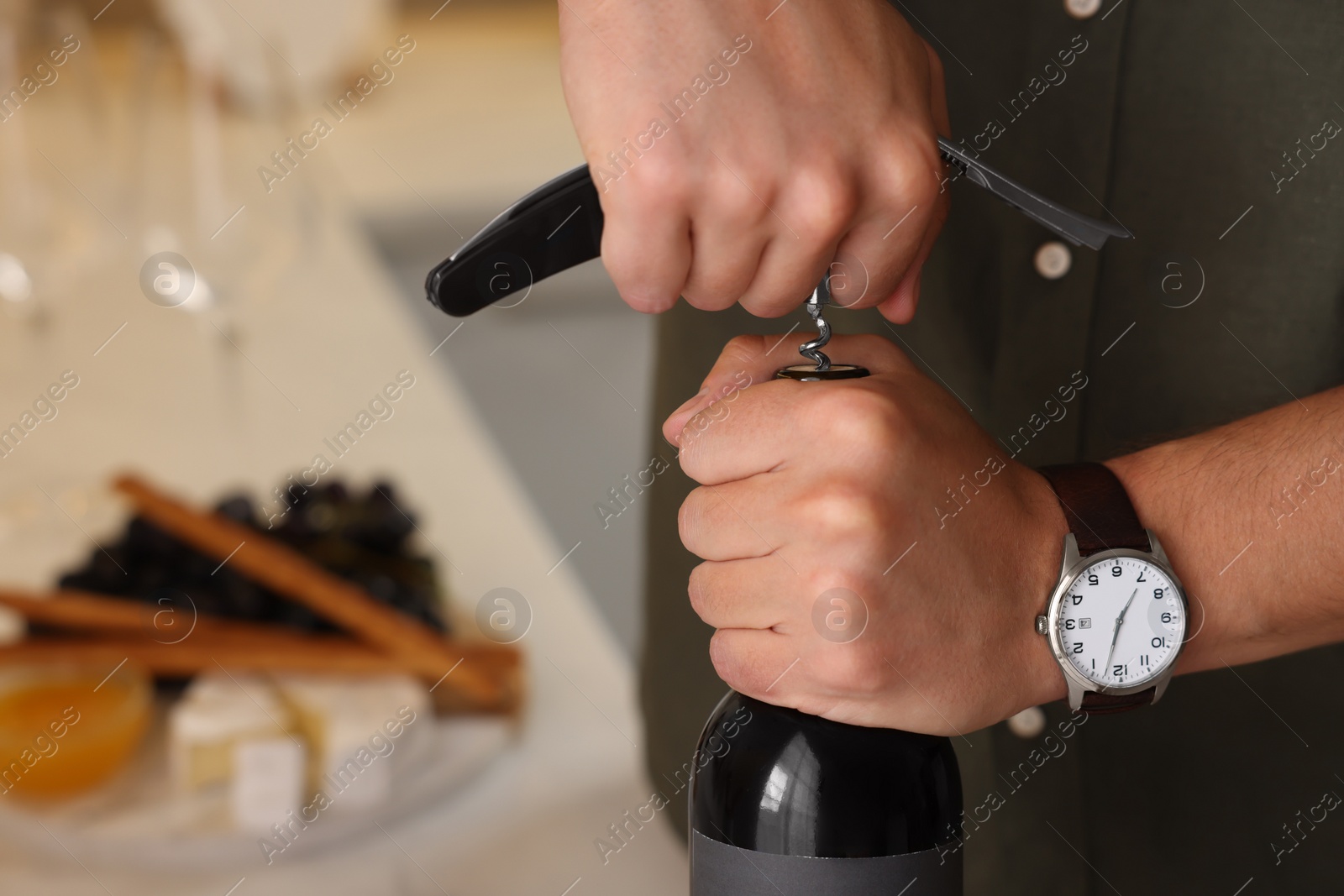 Photo of Man opening wine bottle with corkscrew indoors, closeup. Space for text