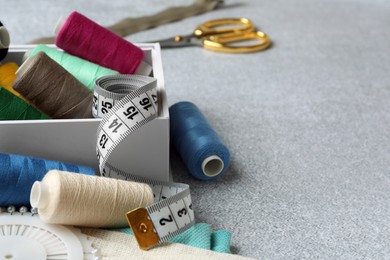 Photo of Spools of threads and sewing tools on light textured table, space for text