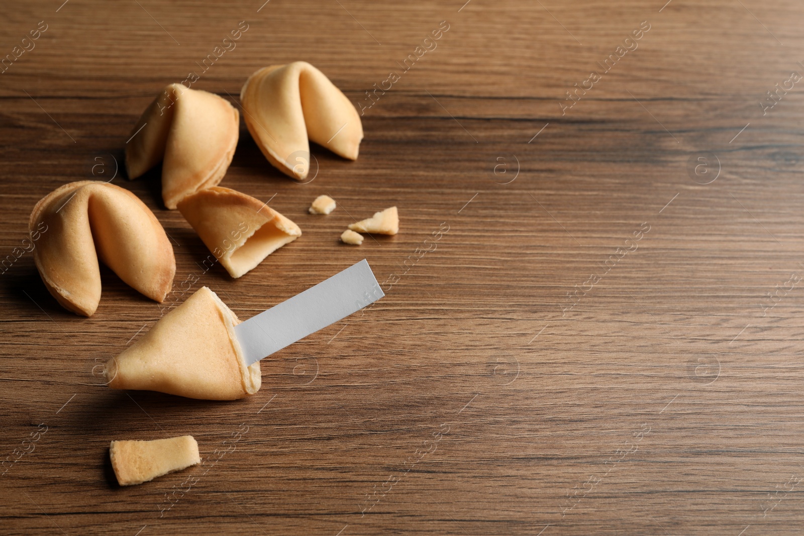 Photo of Tasty fortune cookies and paper with prediction on wooden table, space for text