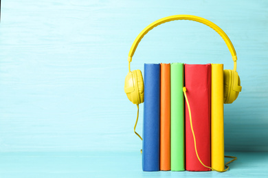 Books and modern headphones on light blue wooden table. Space for text