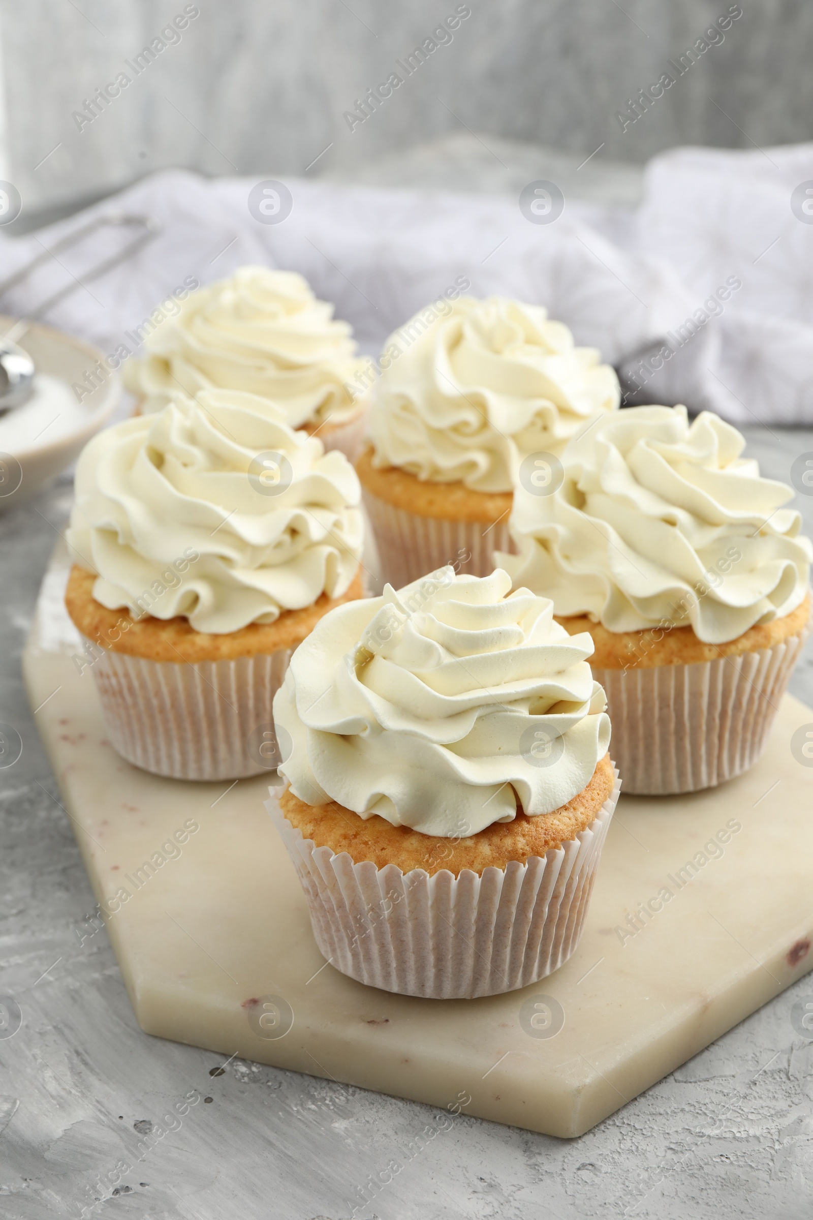 Photo of Tasty cupcakes with vanilla cream on grey table, closeup