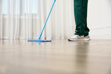 Photo of Professional janitor cleaning parquet floor with mop indoors, closeup