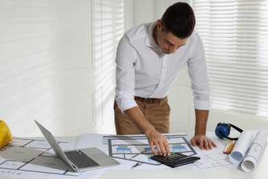 Photo of Architect working with construction drawings and calculator in office