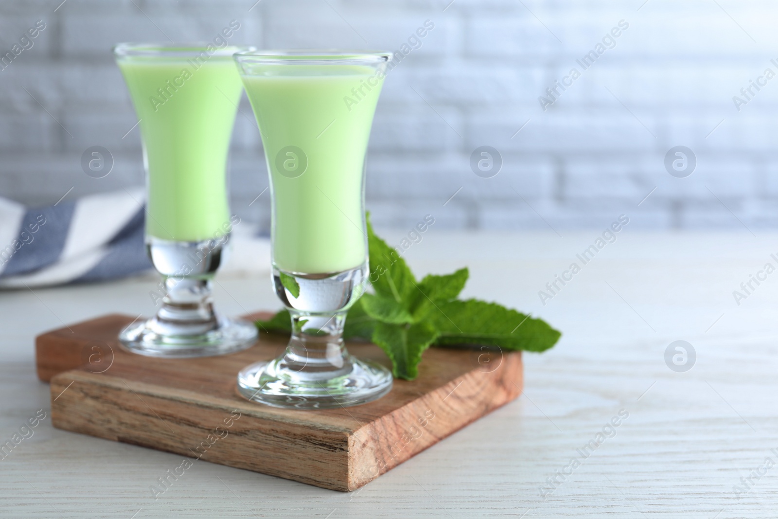 Photo of Delicious mint liqueur on white wooden table, closeup. Space for text