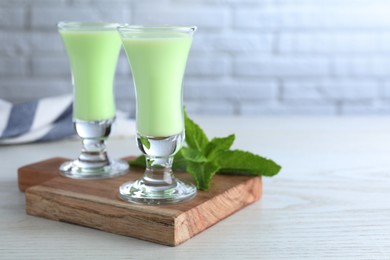 Photo of Delicious mint liqueur on white wooden table, closeup. Space for text