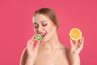 Young woman with cut kiwi and orange on pink background. Vitamin rich food