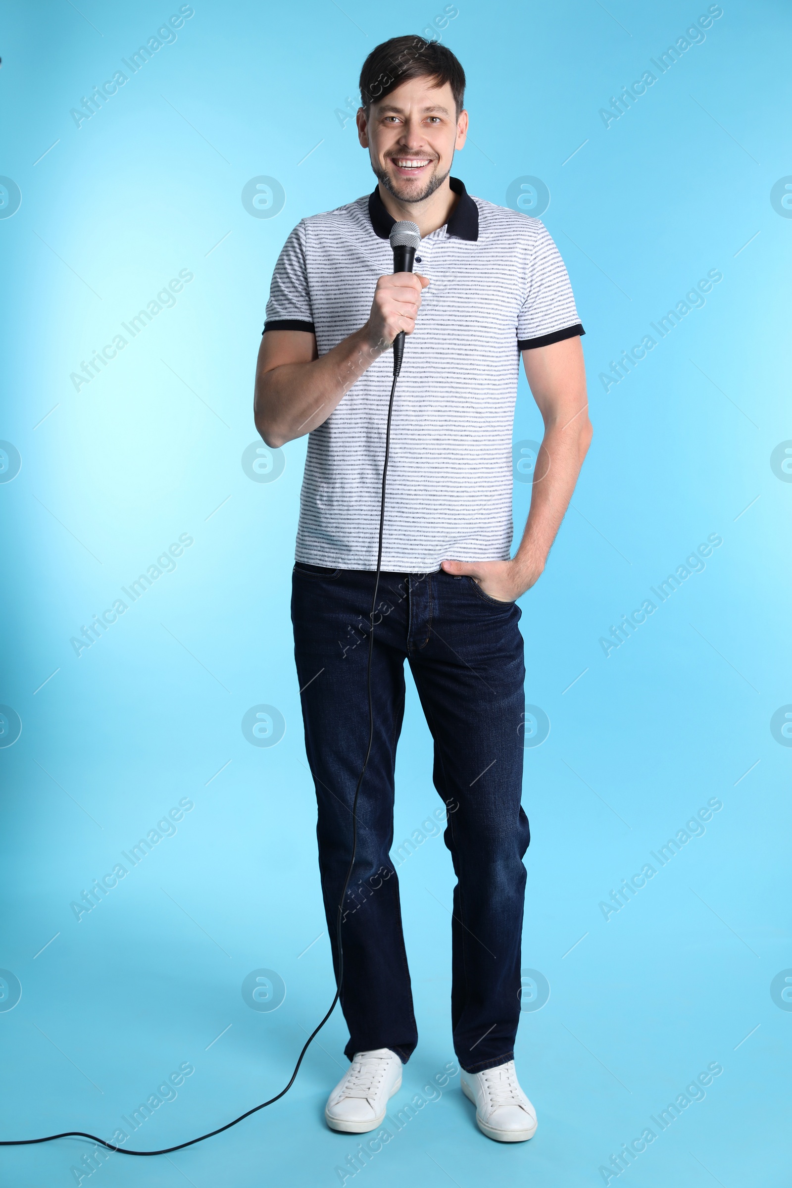 Photo of Handsome man in casual clothes posing with microphone on color background