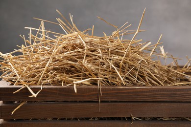 Dried straw in wooden crate against grey background, closeup