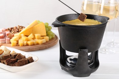 Photo of Dipping piece of bread into fondue pot with tasty melted cheese at white wooden table, closeup