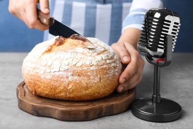 Photo of Woman making ASMR sounds with microphone and bread at grey table, closeup