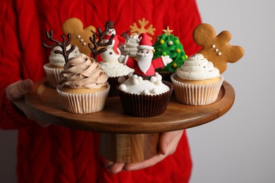 Photo of Woman holding tasty Christmas cupcakes on light background, closeup