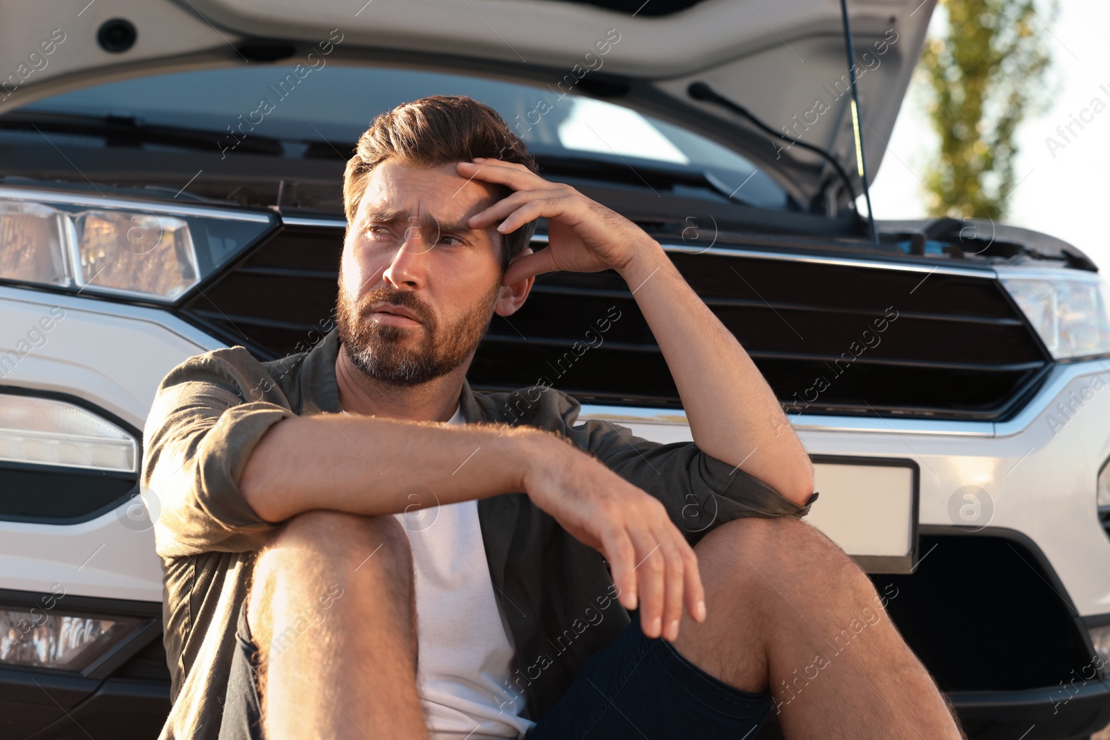 Photo of Upset man sitting near broken car outdoors