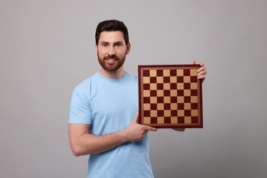 Photo of Smiling man holding chessboard on light grey background
