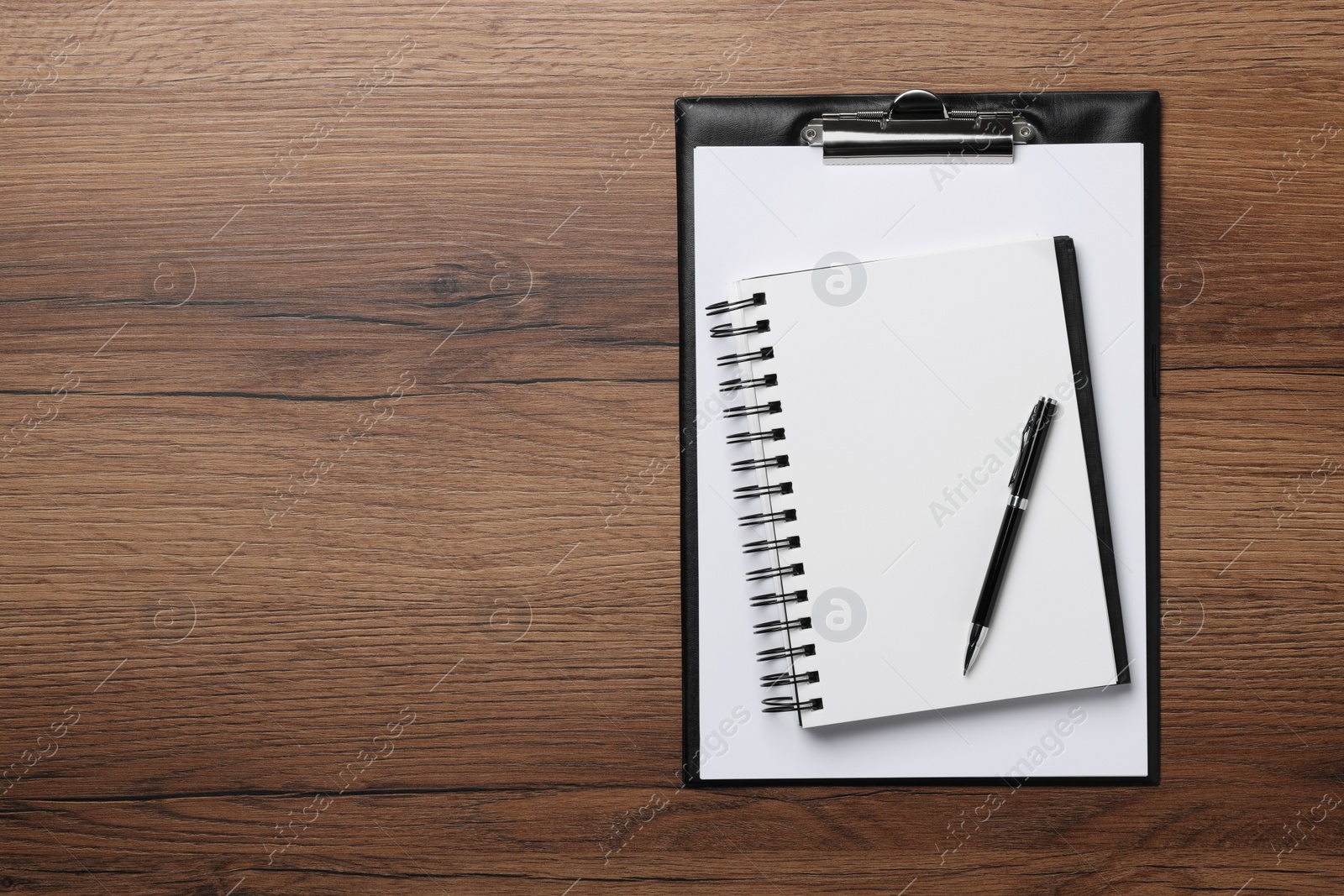 Photo of Ballpoint pen, notebook and clipboard with paper sheet on wooden table, flat lay. Space for text