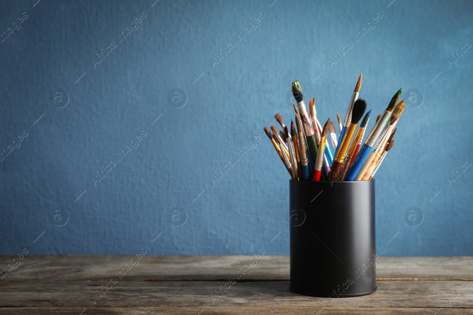 Photo of Holder with paint brushes on table against color background. Space for text