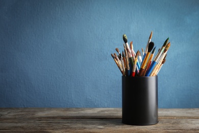 Photo of Holder with paint brushes on table against color background. Space for text