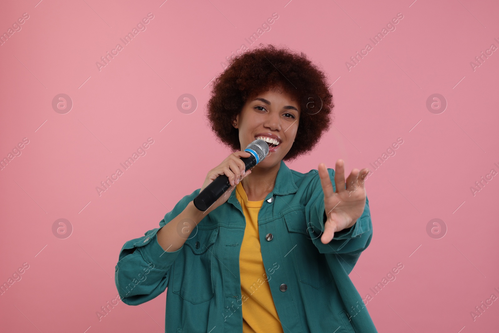 Photo of Curly young woman with microphone singing on pink background