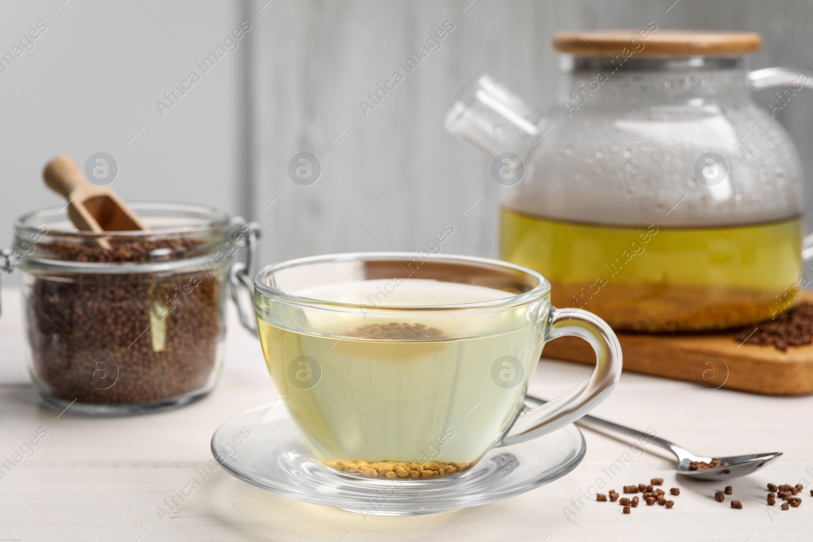 Photo of Cup of buckwheat tea, hot teapot and granules on white wooden table