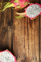 Photo of Delicious cut and whole dragon fruits (pitahaya) on wooden table, flat lay. Space for text