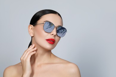 Image of Attractive woman in stylish sunglasses on light grey background. Palm leaves and sky reflecting in lenses. Space for text