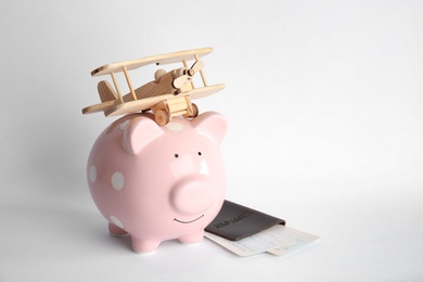 Photo of Piggy bank with toy airplane, passport and tickets on white background, space for text. Travel agency